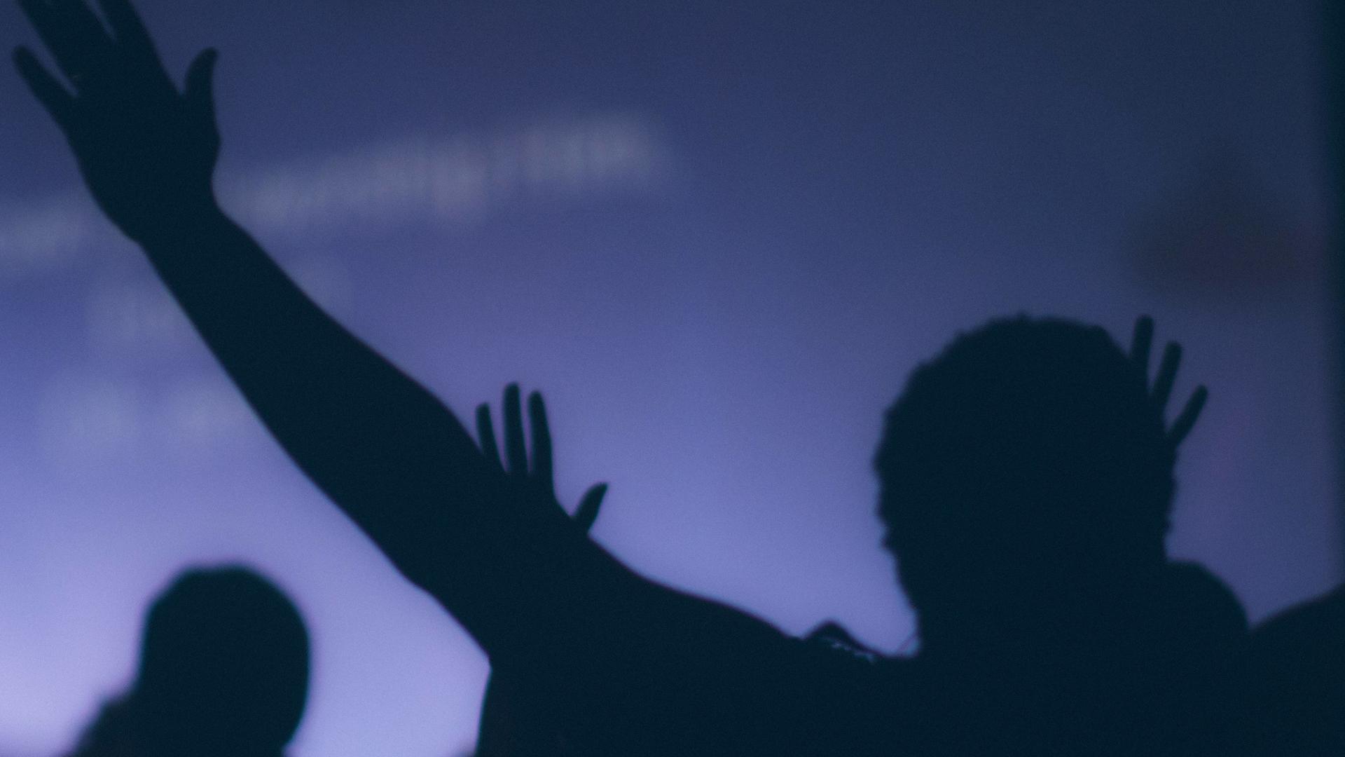 silhouette of people with hands in the air in front of projected screen